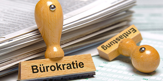 Zwei Stempel mit Aufdruck Bürokratie und Entlastung neben einen Aktenstapel